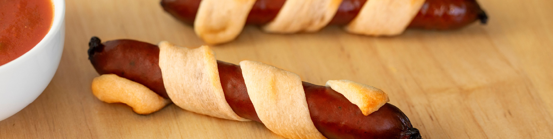 Meat sticks wrapped in dough with bowl of dipping sauce