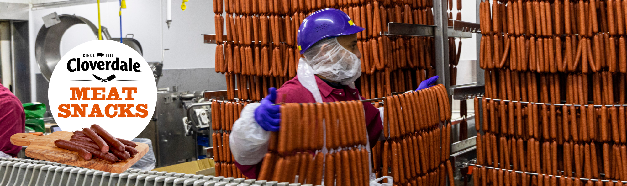 Meat snacks hanging on racks in processing plant with worker holding rack